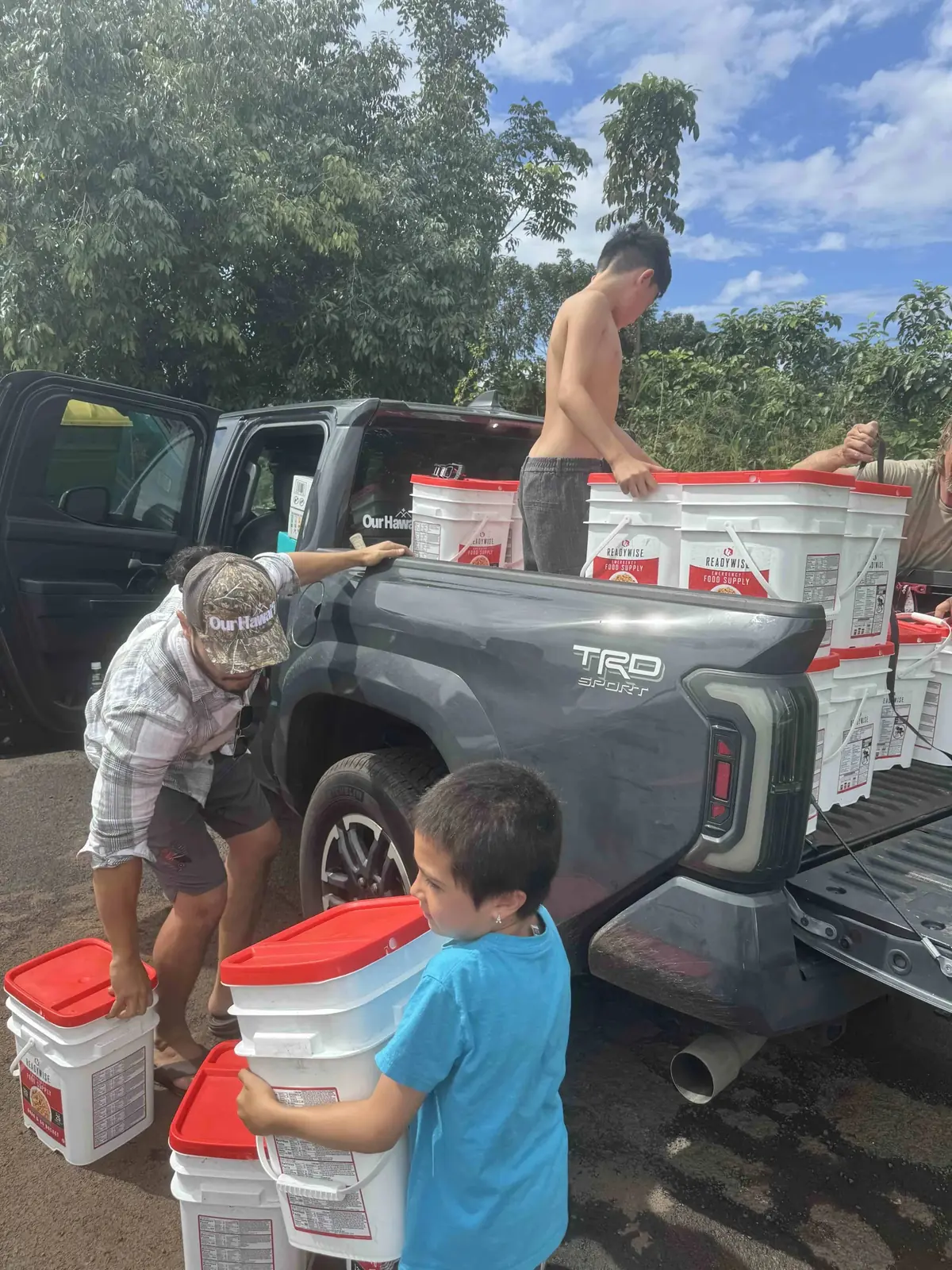 A keiki helps unload buckets of supplies from a truck